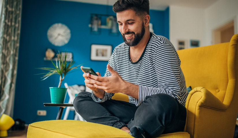 Man on a couch looking down smiling at a cellphone