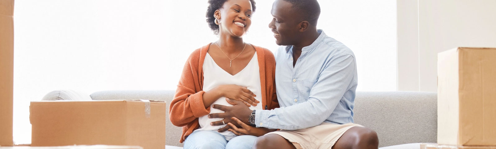 Couple sitting on a couch with the man holding his hand on the pregnant woman's stomach